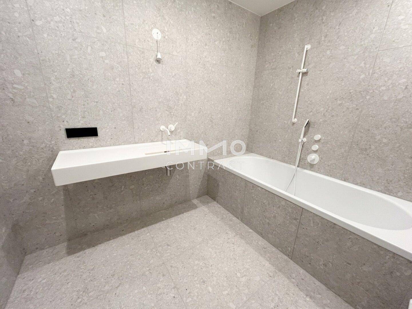 Modernes Badezimmer mit grauen Fliesen, integrierter Badewanne und schwebendem Waschbecken.