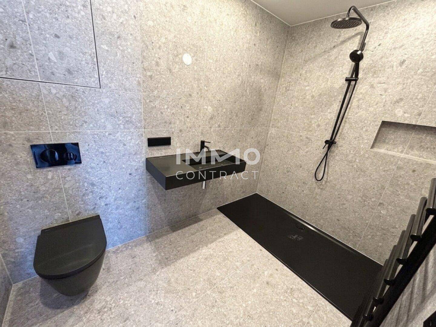 Modernes Badezimmer mit grauen Fliesen, ebenerdiger Dusche und schwarzen Armaturen.