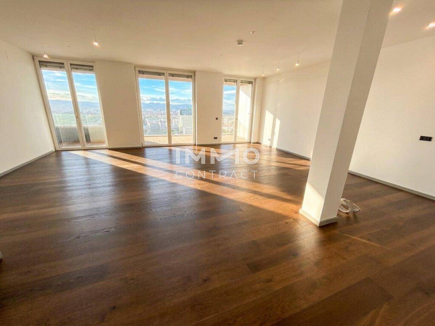 Geräumiges, leeres Wohnzimmer mit dunklem Holzboden und großen Fenstern mit Stadtblick.