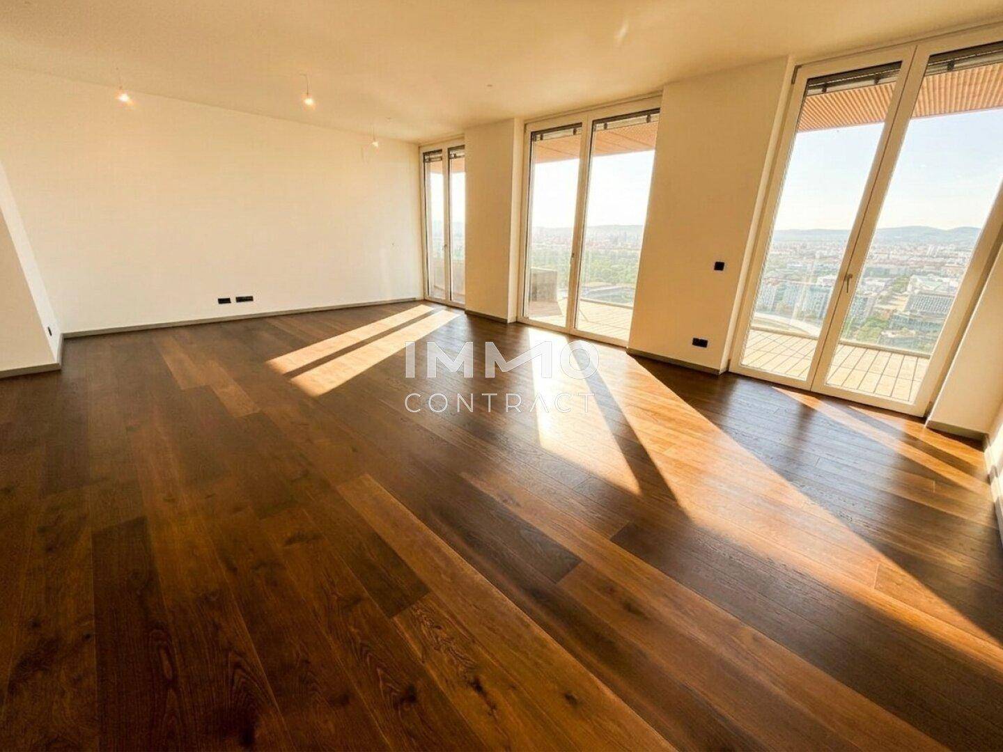 Helles, leeres Zimmer mit Holzboden und bodentiefen Fenstern, die einen weiten Stadtblick bieten.