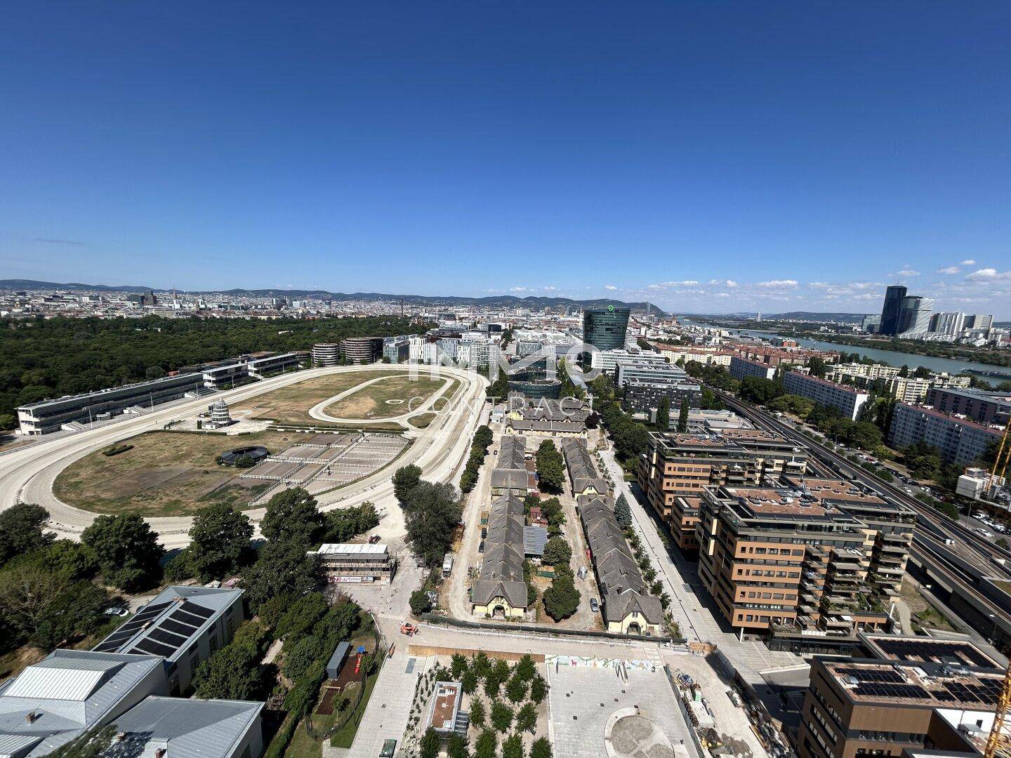 Panoramablick auf die Stadt mit Rennbahn, Gebäuden und der Donau unter blauem Himmel.