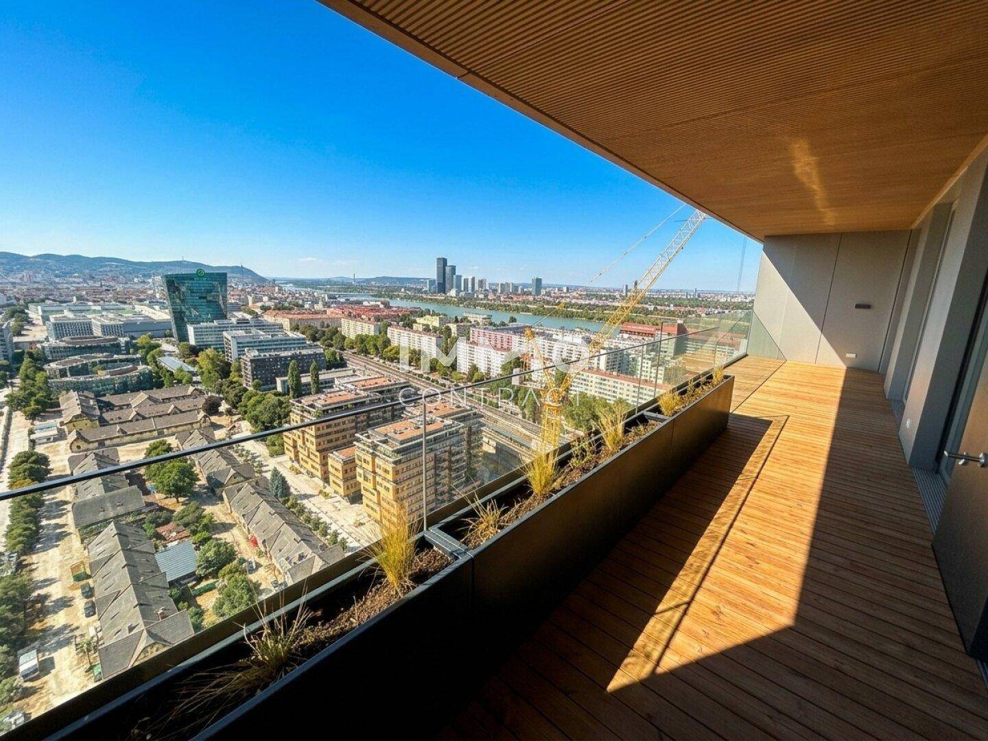 Geräumiger Holzbalkon mit Pflanzenkübeln und beeindruckendem Stadtpanorama unter strahlendem Himmel.