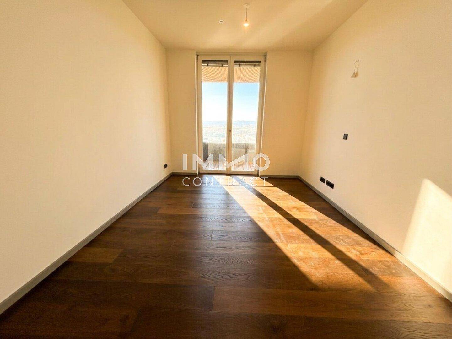 Helles, leeres Schlafzimmer mit Holzboden und Zugang zu einem Balkon mit Stadtblick.