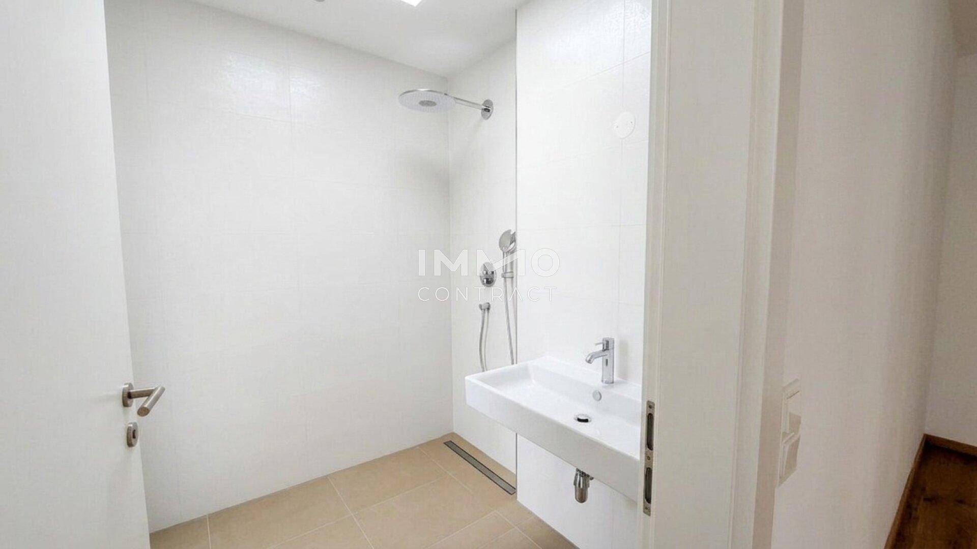Modernes Badezimmer mit ebenerdiger Dusche, Wandwaschbecken und weißen Fliesen.