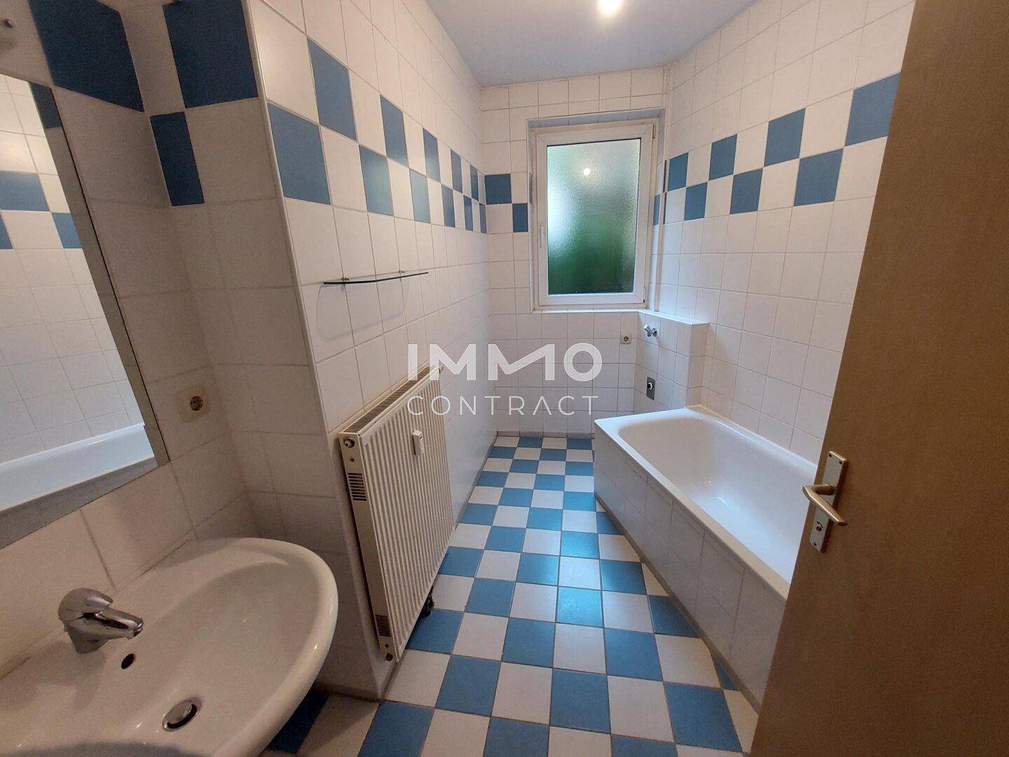 Badezimmer mit Badewanne, Waschbecken, Heizkörper und einem Fenster, gefliest in Blau und Weiß.