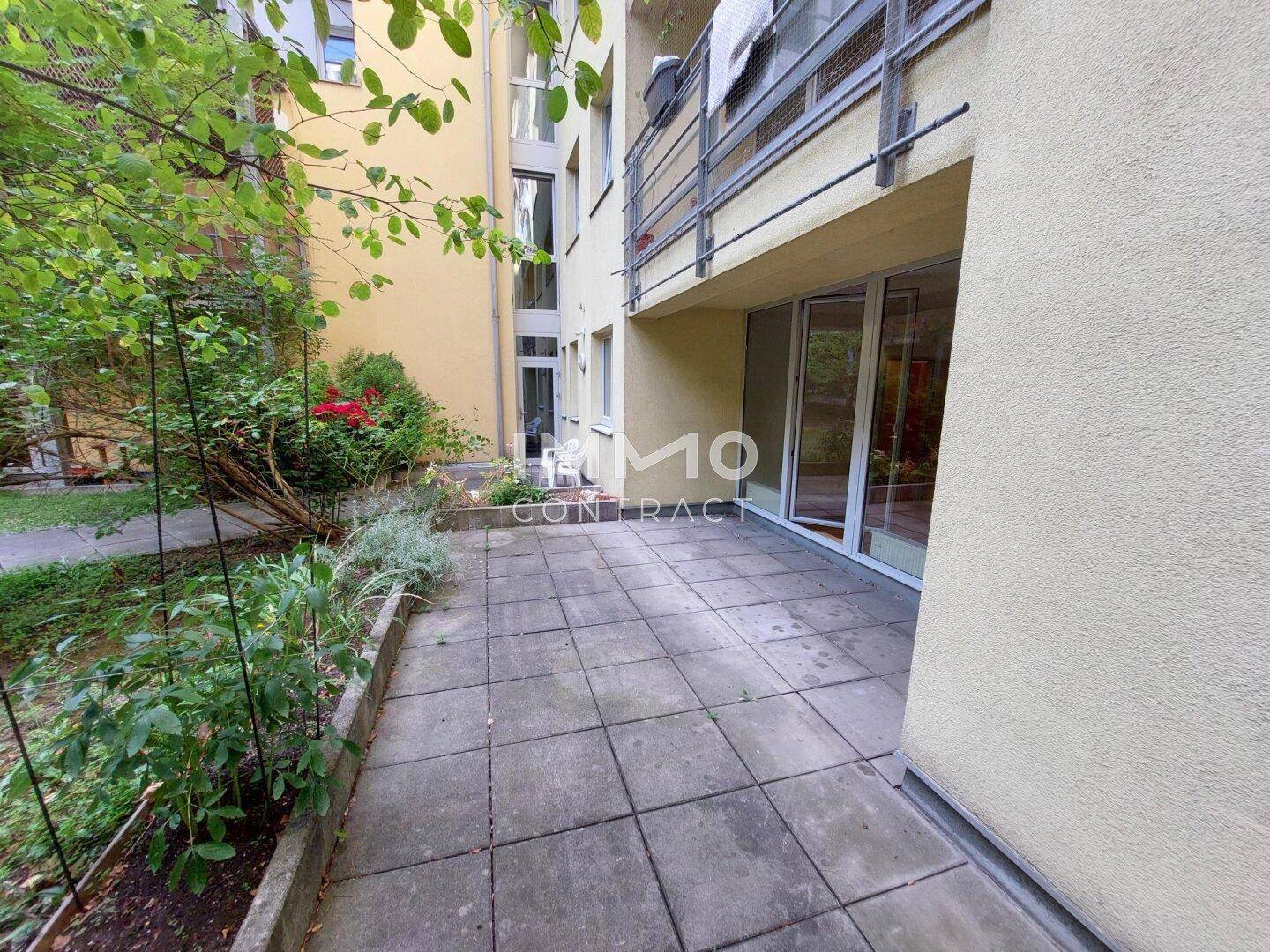 Gepflasterte Terrasse mit Grünflächen und direktem Zugang zum Wohnbereich des Gebäudes.