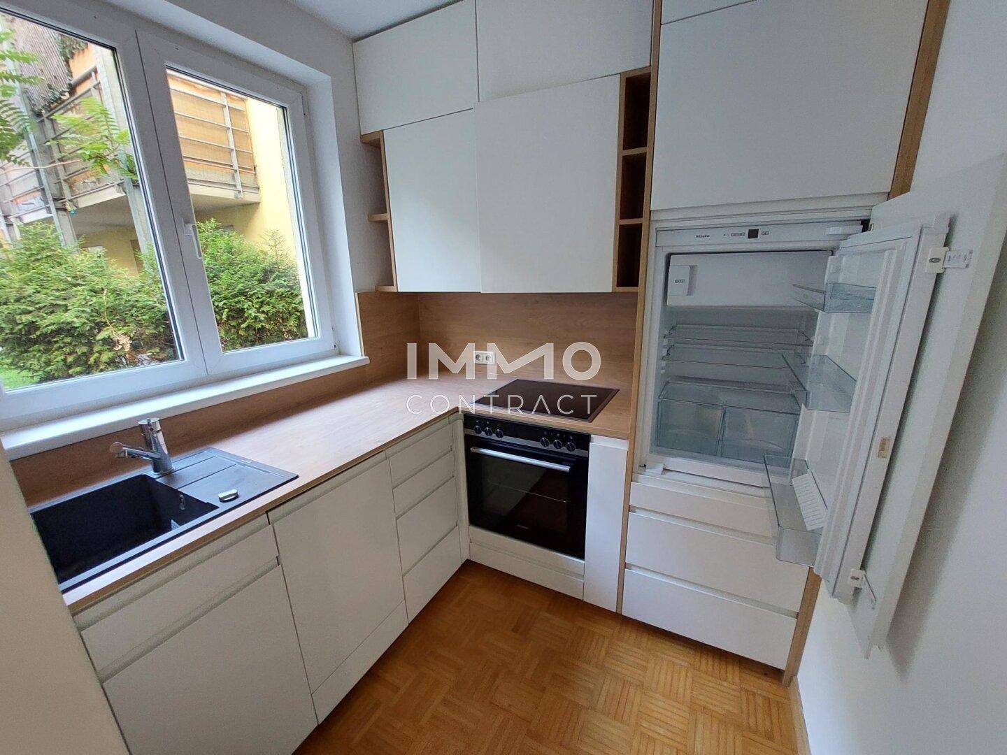 Kompakte Küche mit integriertem Kühlschrank, weißen Schränken und praktischer Holzarbeitsplatte.