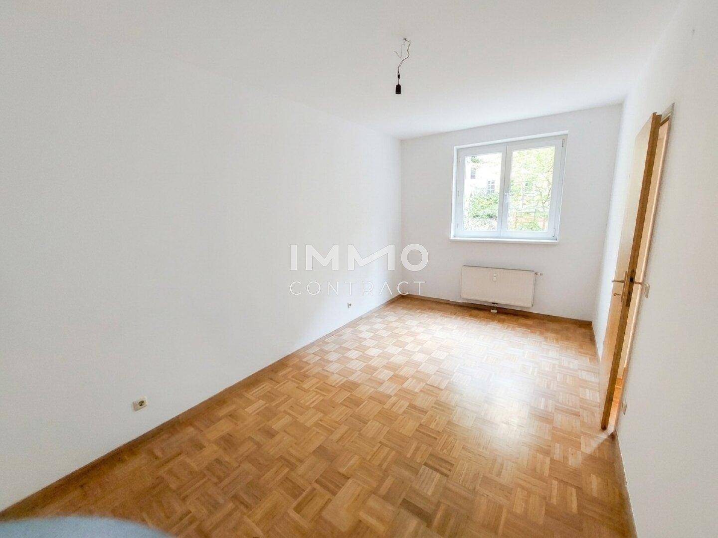 Helles Schlafzimmer mit Parkettboden und einem Fenster, das den Raum gut belichtet.