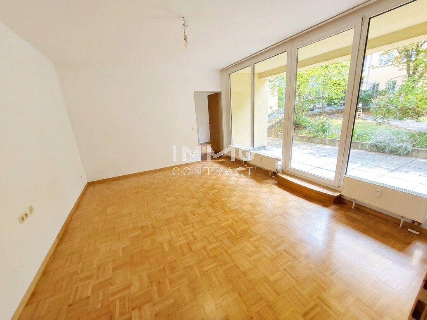 Geräumiges Wohnzimmer mit Parkettboden und großen Fenstern, die viel Tageslicht hereinlassen.