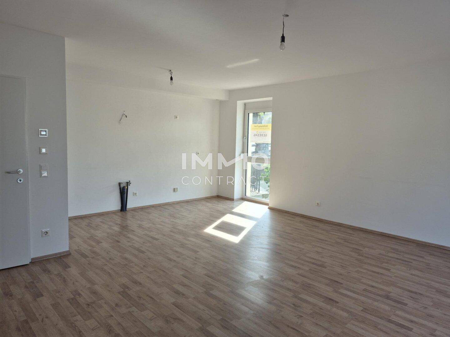 Geräumiges, helles Wohnzimmer mit Laminatboden und Zugang zu einem Außenbereich.