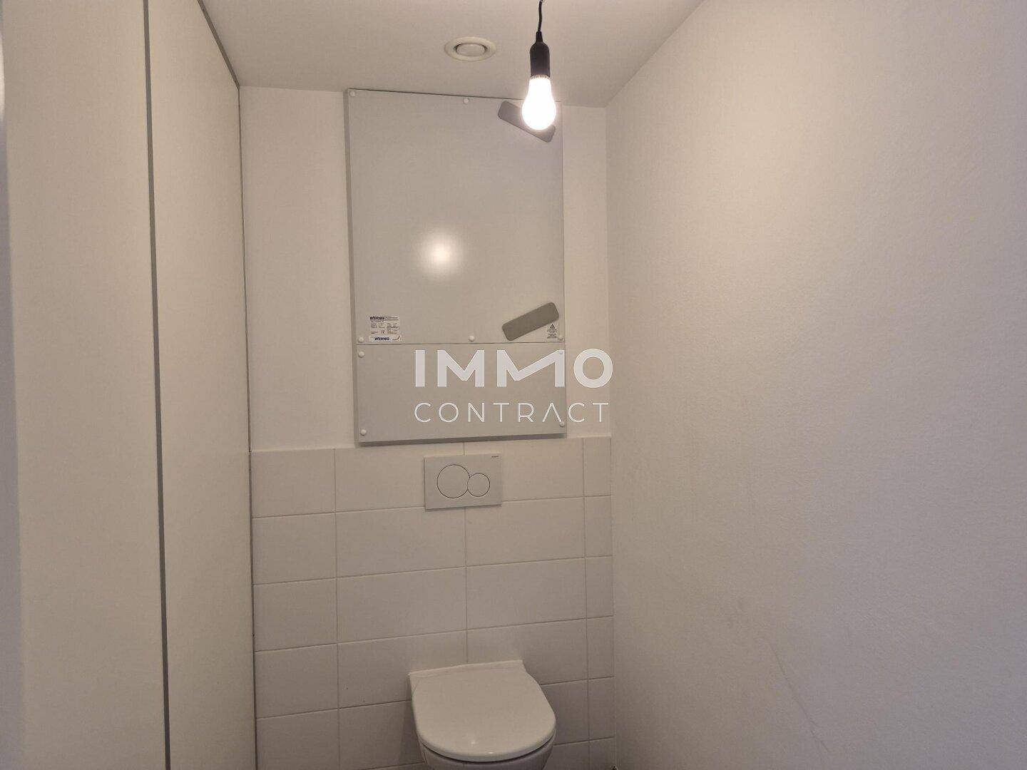 Separates WC mit wandhängender Toilette und weißen Fliesen im unteren Bereich.