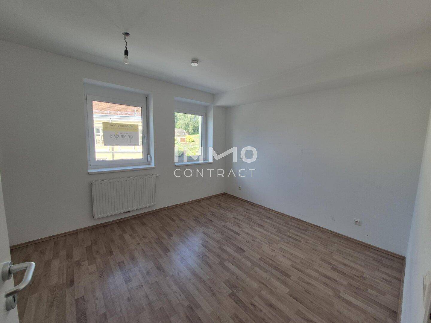 Helles Schlafzimmer mit Laminatboden, Heizkörper unter dem Fenster und Blick ins Grüne.