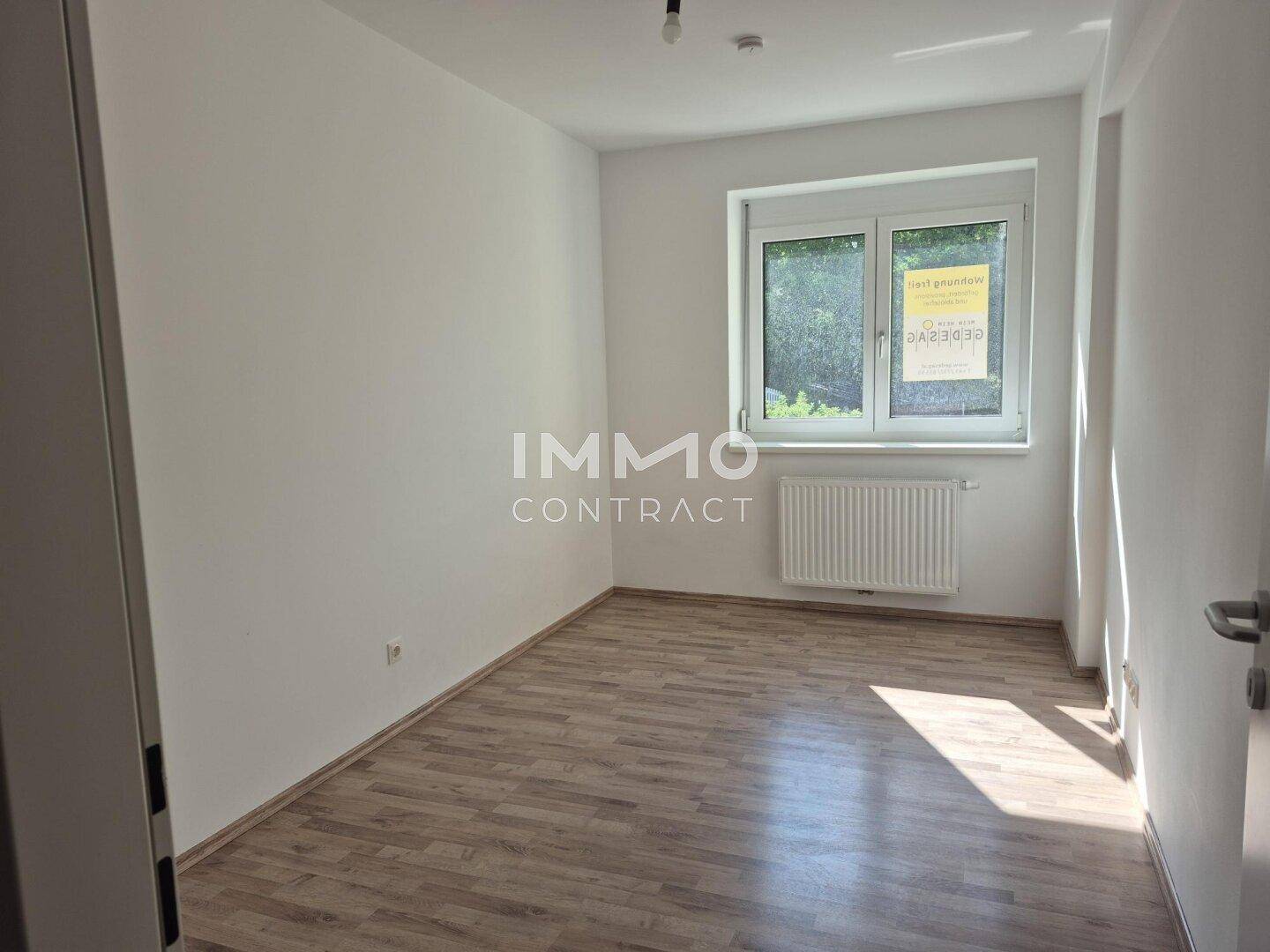 Helles Schlafzimmer mit Laminatboden und großem Fenster, das viel natürliches Licht hereinlässt.