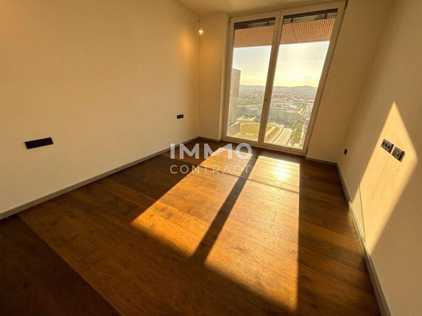 Helles, unmöbliertes Zimmer mit Holzboden und großen Fenstern, durchflutet von Sonnenlicht.