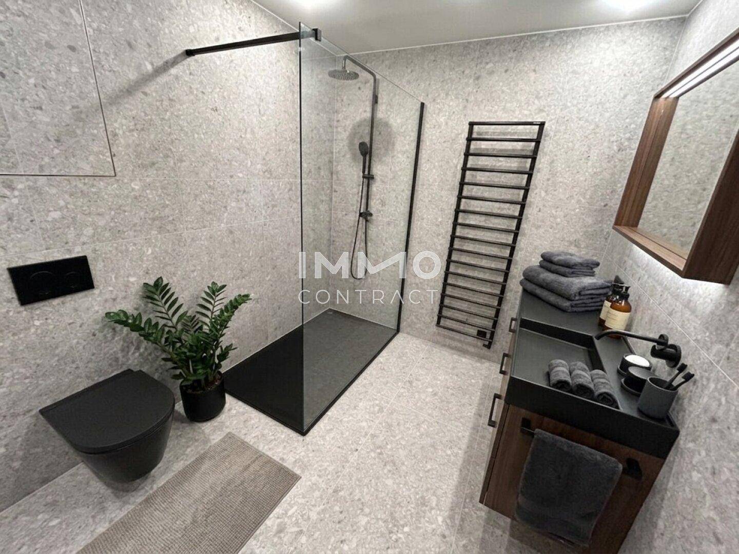 Modernes Badezimmer mit grauen Fliesen, begehbarer Dusche und schwarzer Ausstattung.