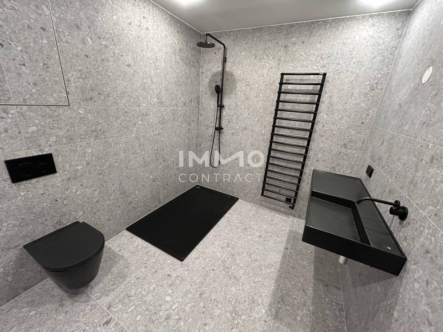 Minimalistisches Badezimmer mit grauen Fliesen, begehbarer Dusche und schwarzer Keramik.