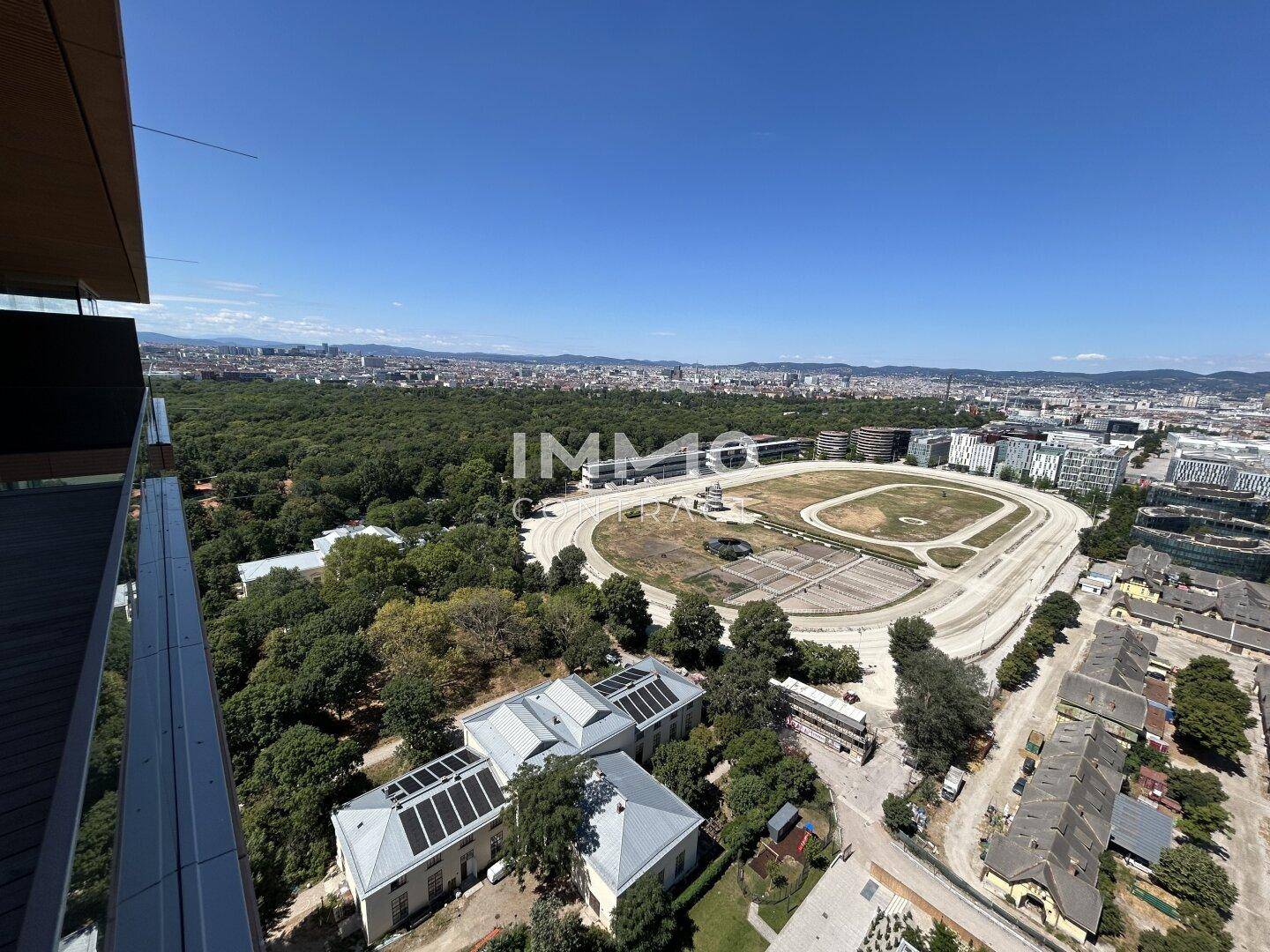 Weitläufiger Blick über die Stadt, grüne Parkanlagen und eine Pferderennbahn.