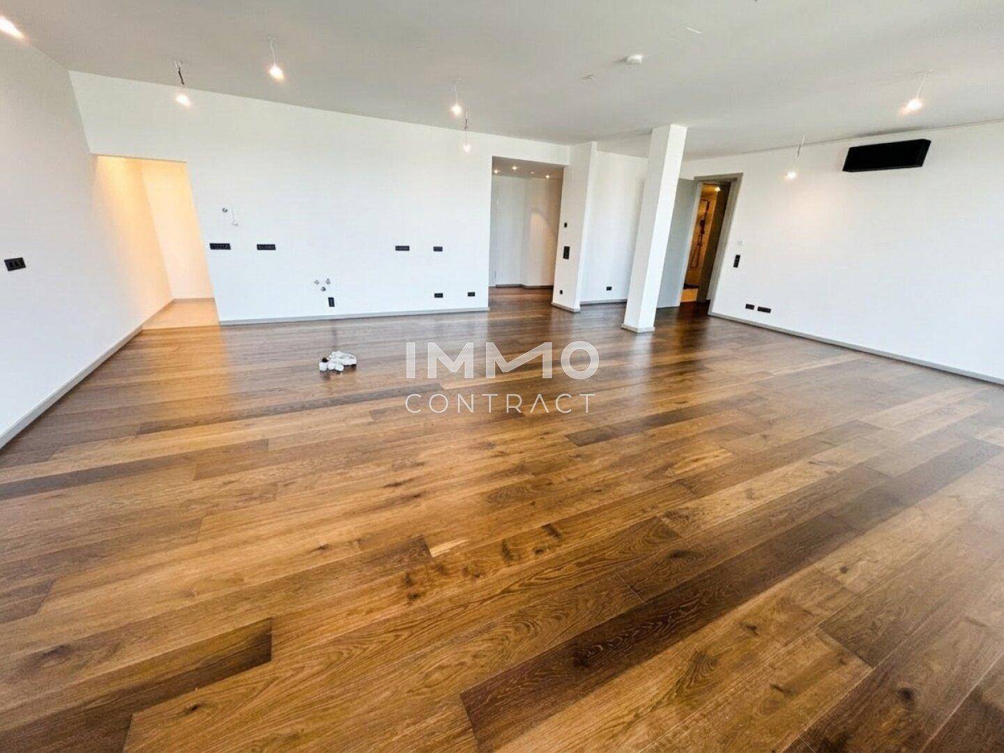 Geräumiger, unmöblierter Wohnbereich mit elegantem Holzboden und weißen Wänden.