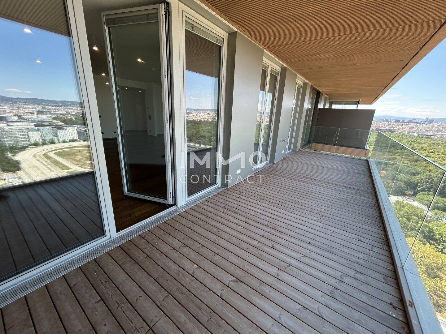 Langer, unmöblierter Balkon mit Holzboden und Glasgeländer, bietet weite Aussicht.