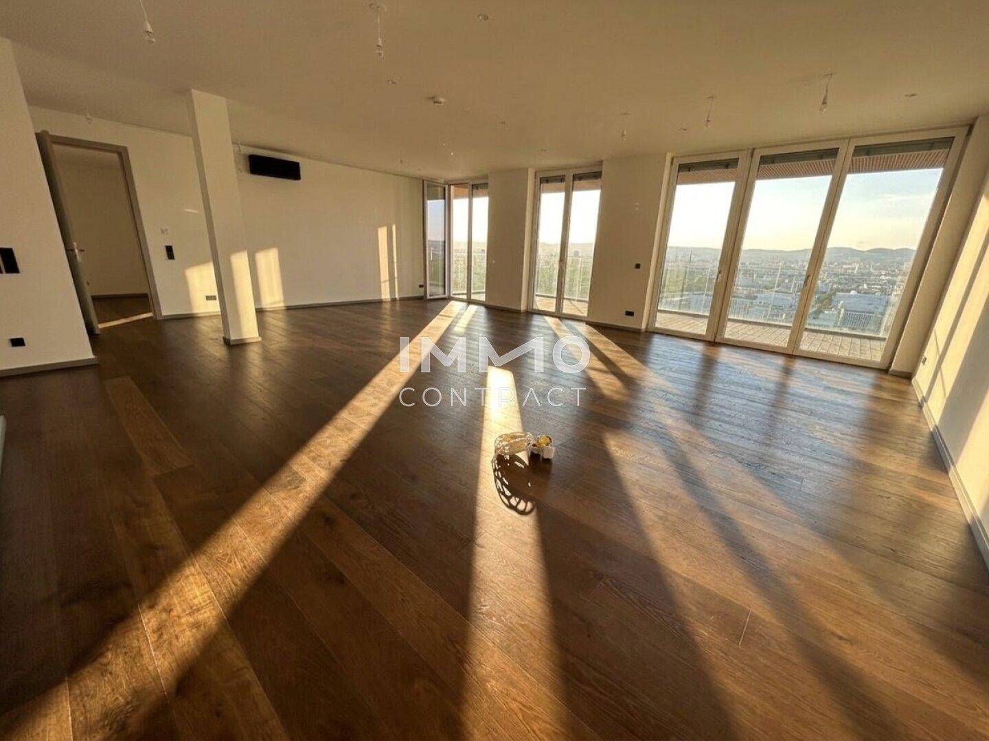 Heller Wohnbereich mit Holzboden und großen Fenstern, durchflutet von Sonnenlicht.