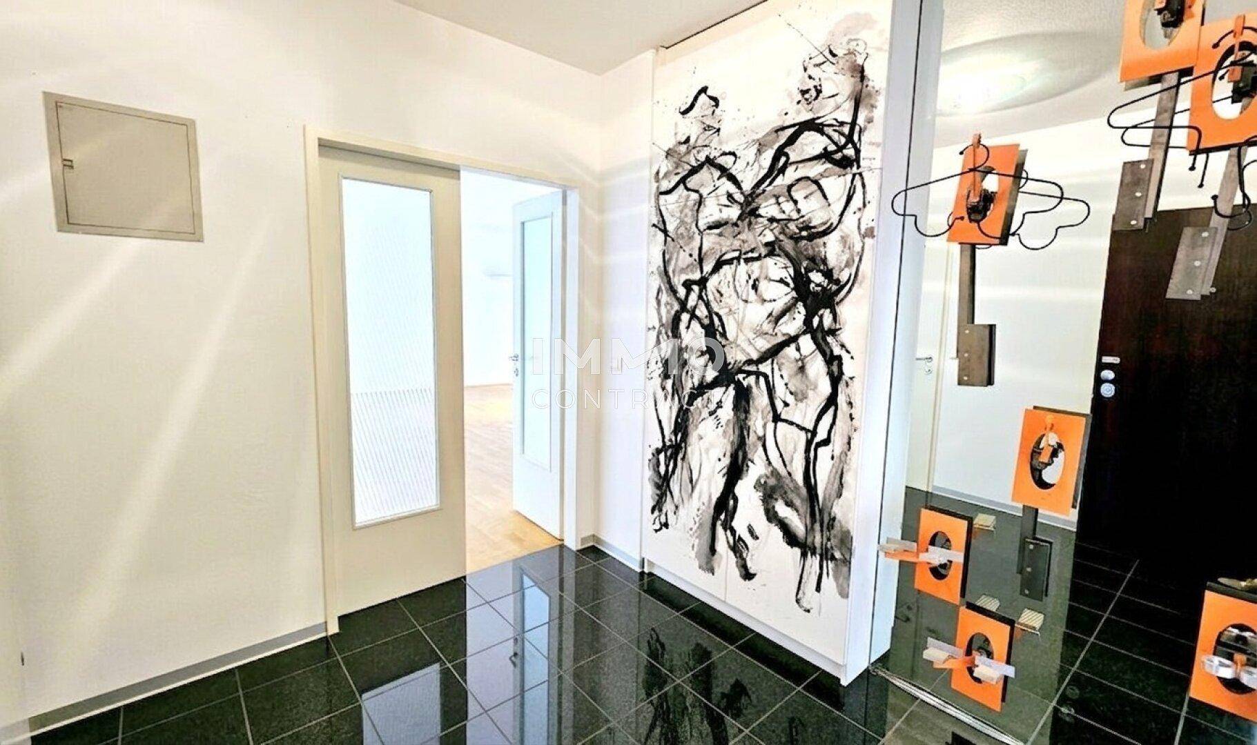 Heller Flur mit dunklem Fliesenboden und moderner Kunst an der Wand.