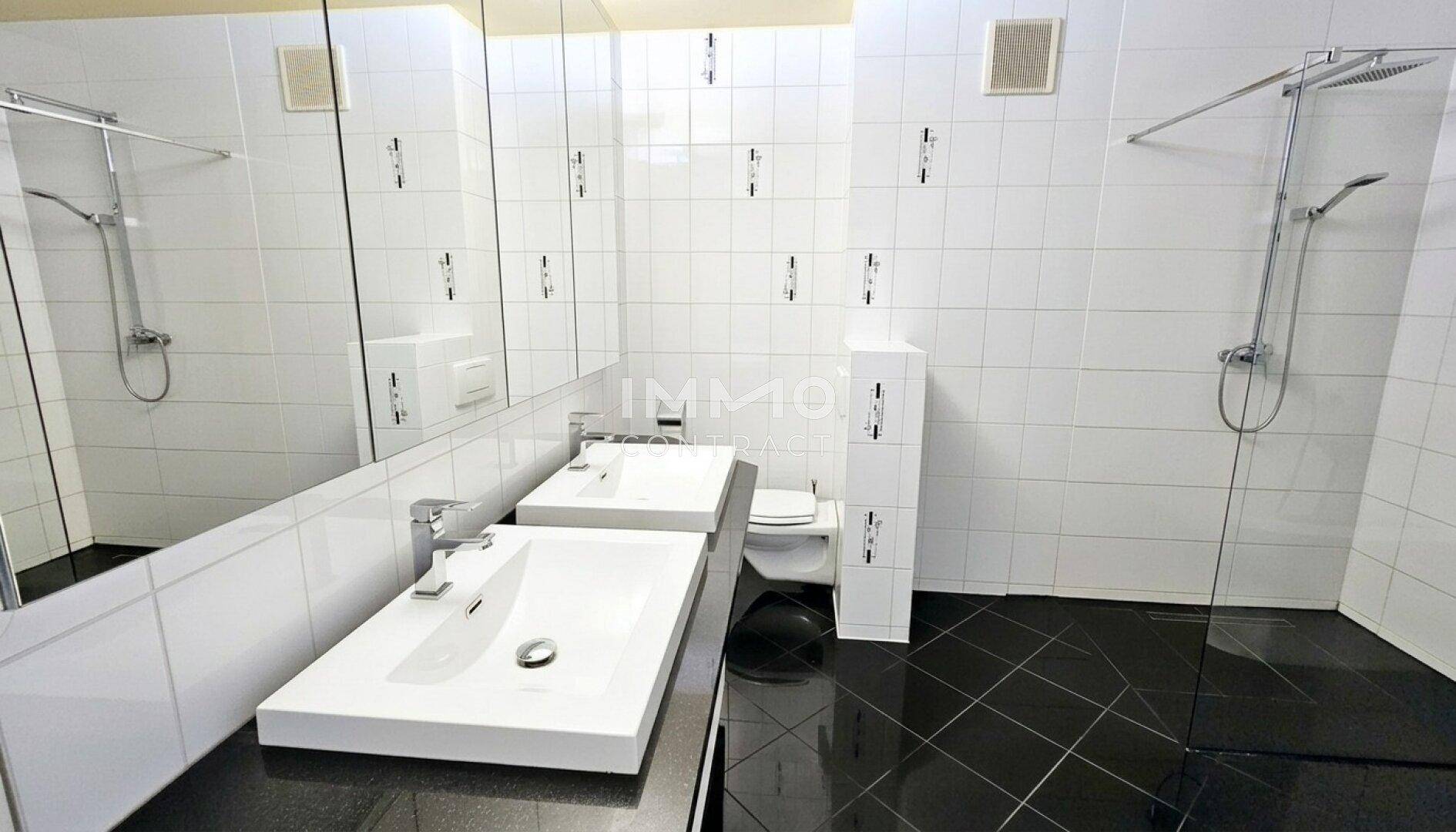 Modernes Badezimmer mit Doppelwaschbecken, Dusche und schwarzen Fliesen.