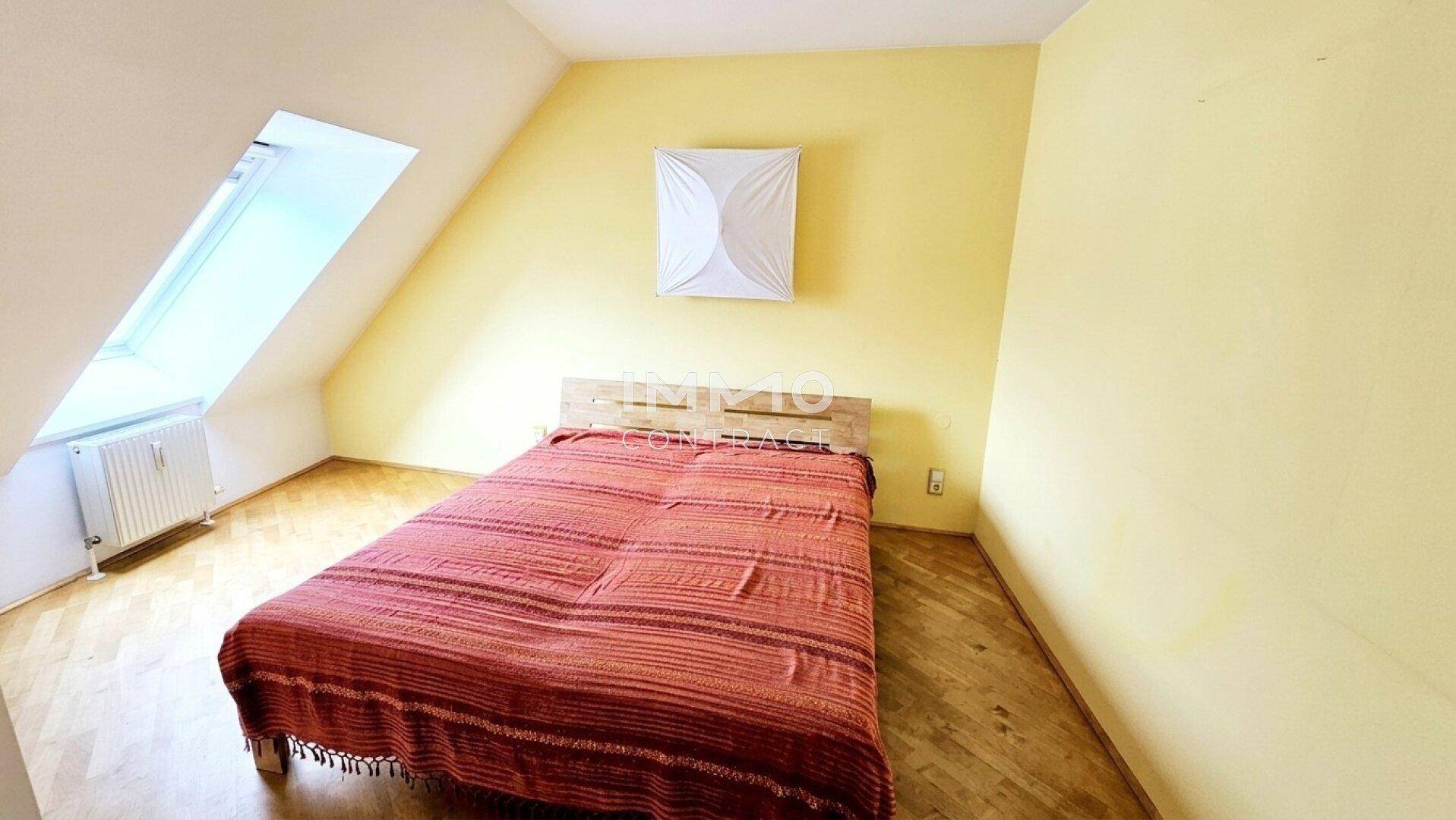 Gemütliches Schlafzimmer im Dachgeschoss mit gelben Wänden, Holzboden und Dachfenster.