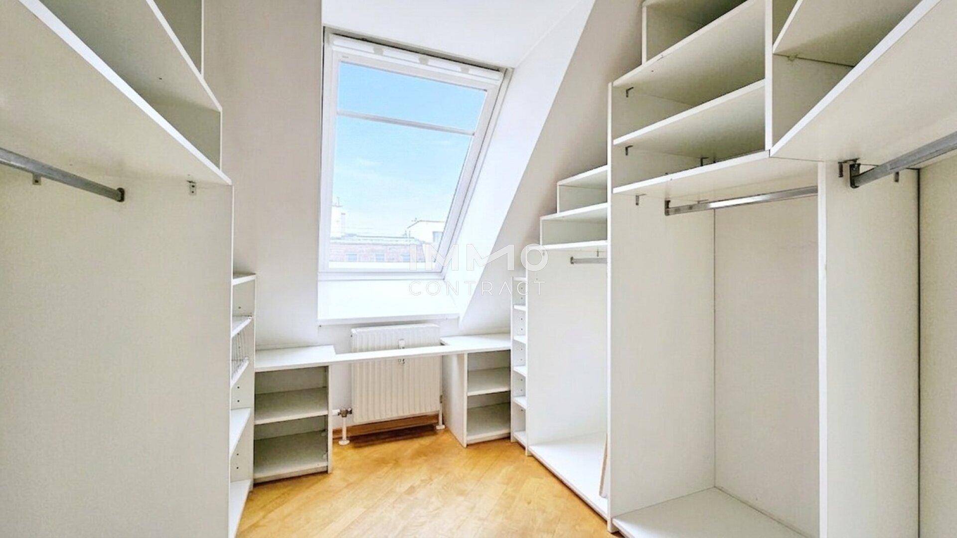 Begehbarer Kleiderschrank mit Regalen und Dachfenster für natürliche Belichtung.