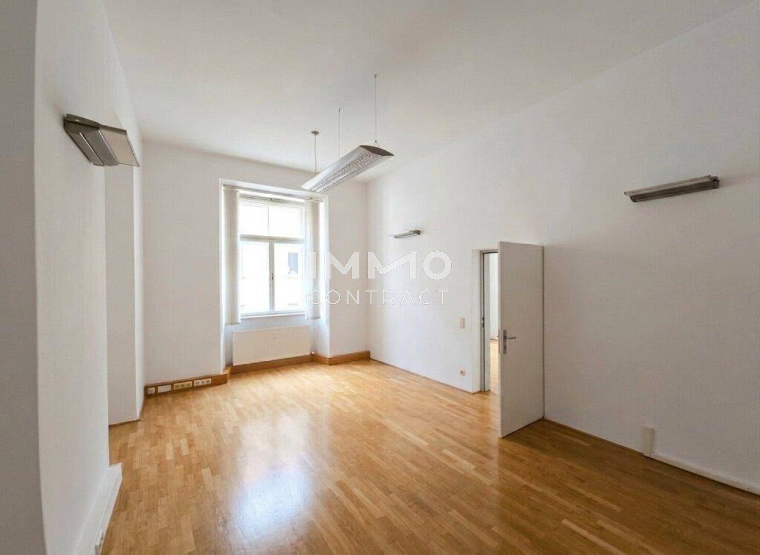 Heller Raum mit Holzboden, großem Fenster und schlichten Wandleuchten.