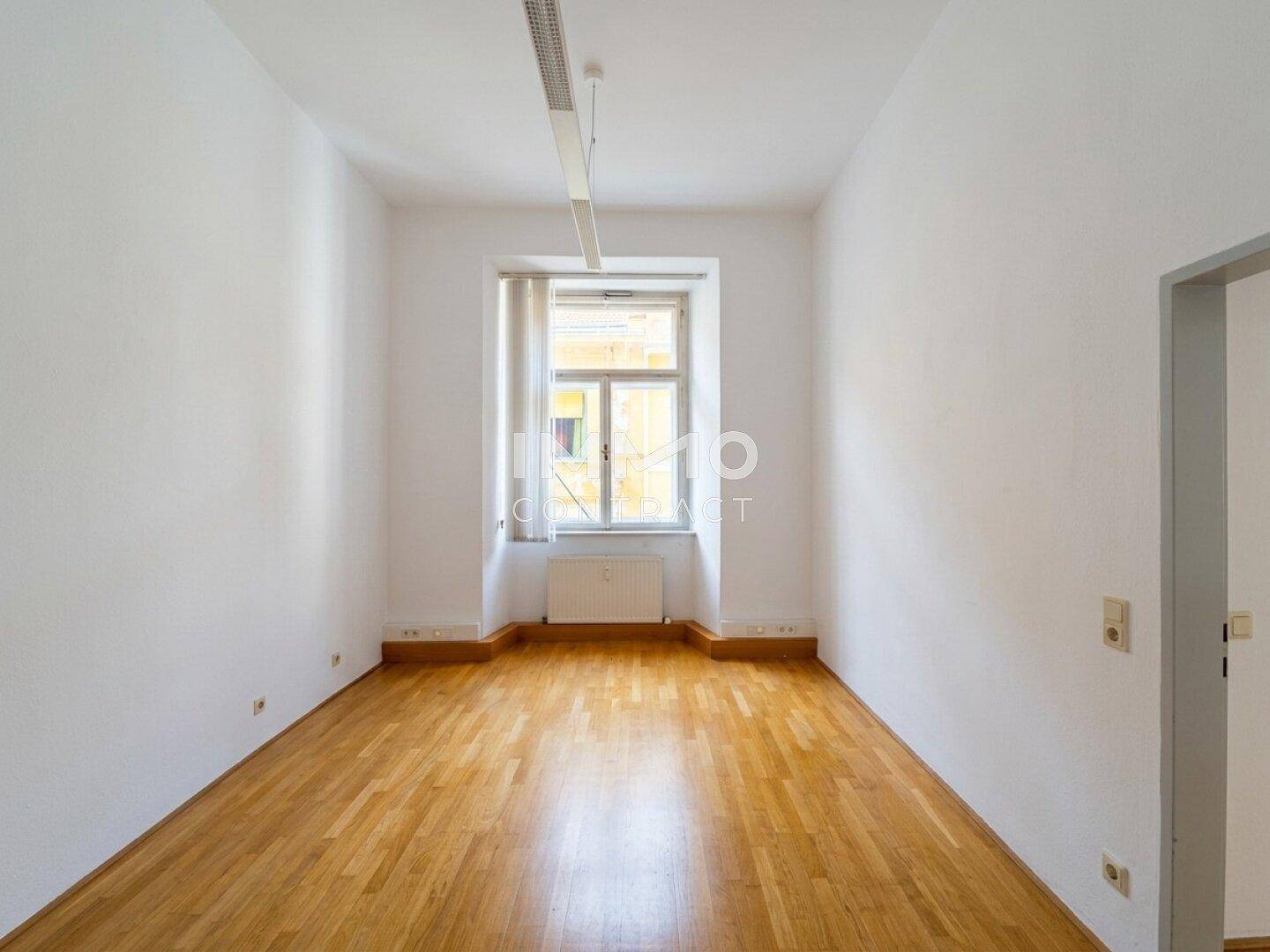 Leerer Raum mit Holzboden, einem Fenster und einer Deckenleuchte.