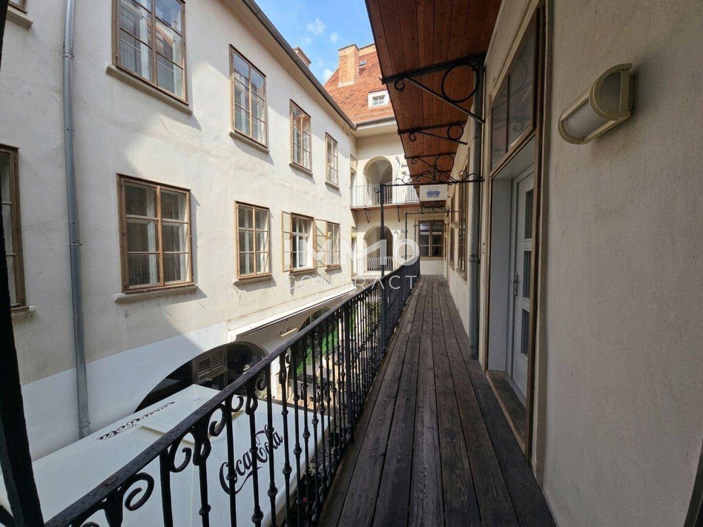 Langer Außenflur mit Holzplanken und schmiedeeisernem Geländer, Blick auf den Innenhof.
