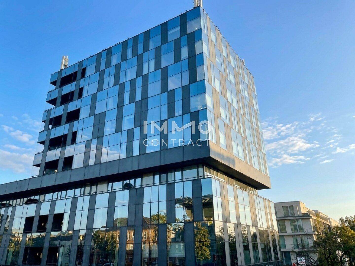 Modernes Bürogebäude mit spiegelnder Glasfassade unter blauem Himmel an einem sonnigen Tag.