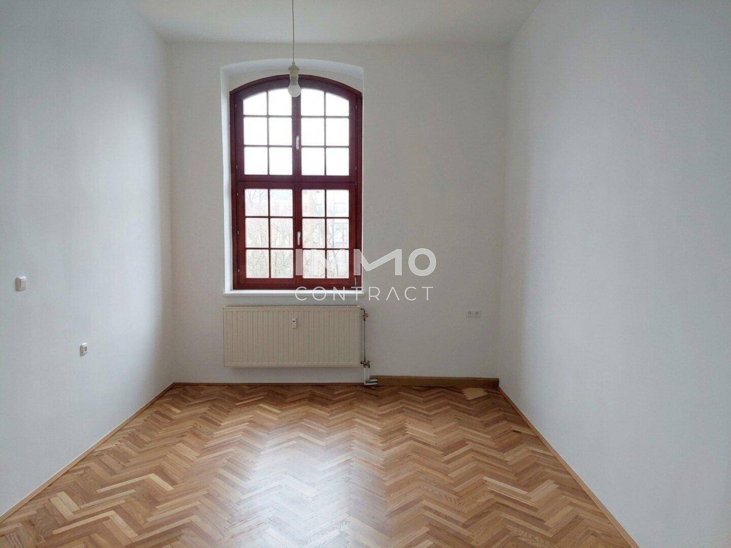 Geräumiges Zimmer mit Fischgrätparkett und einem großen Bogenfenster für viel Tageslicht.