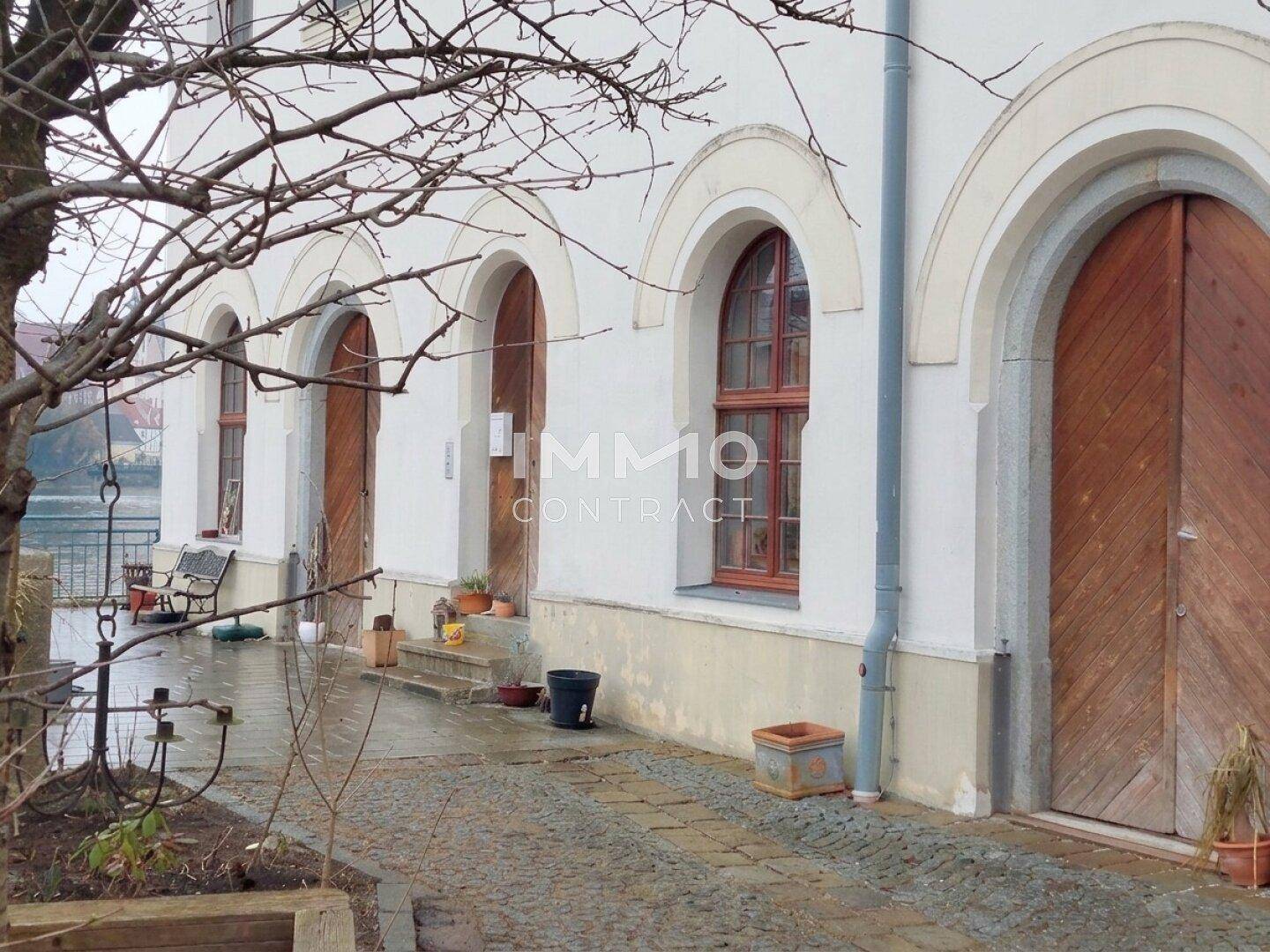 Historische Fassade mit Rundbogenfenstern und Holztüren, direkt am Fluss gelegen.