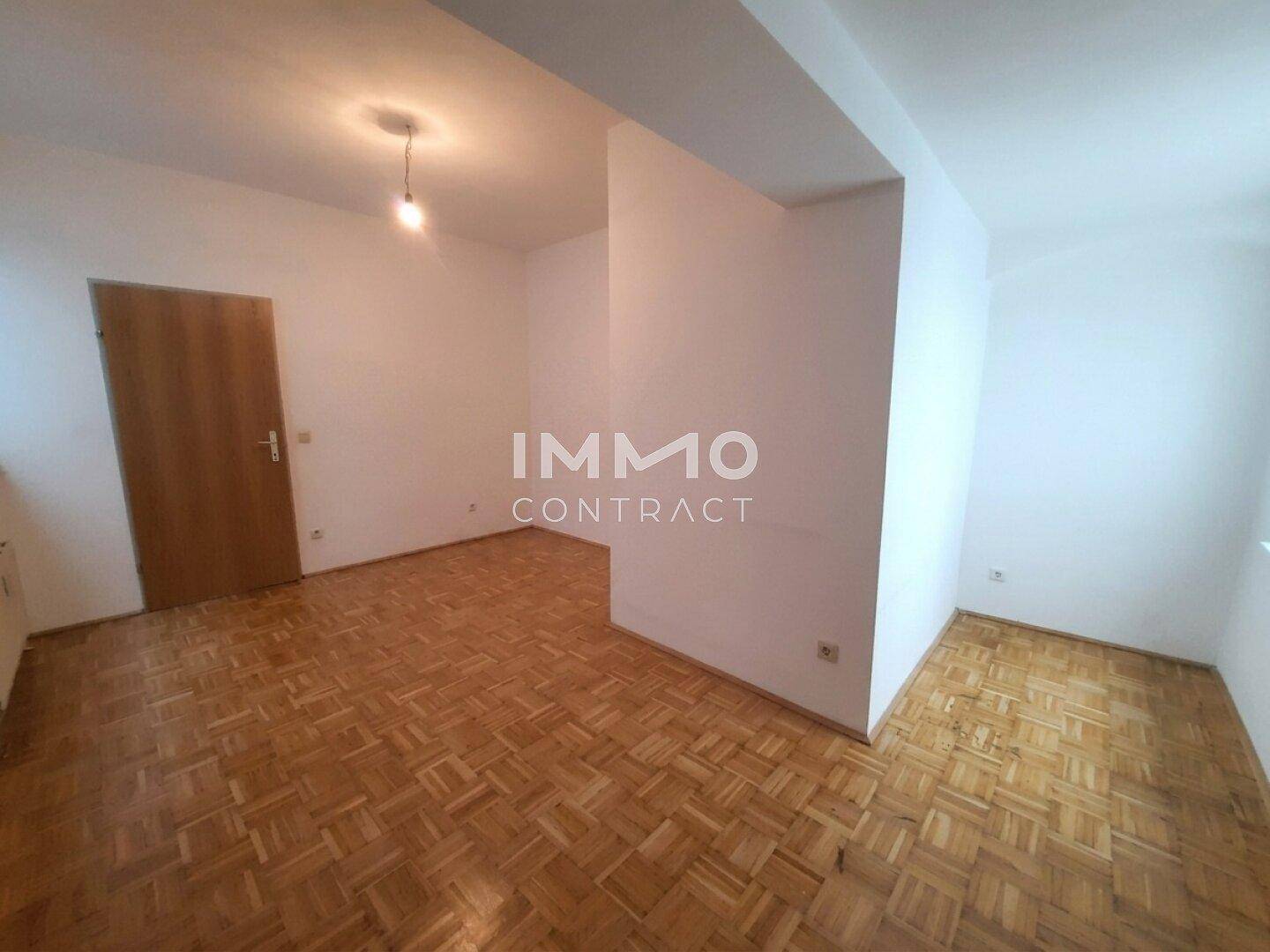 Geräumiger Wohnbereich mit klassischem Parkettboden und weiß gestrichenen Wänden.