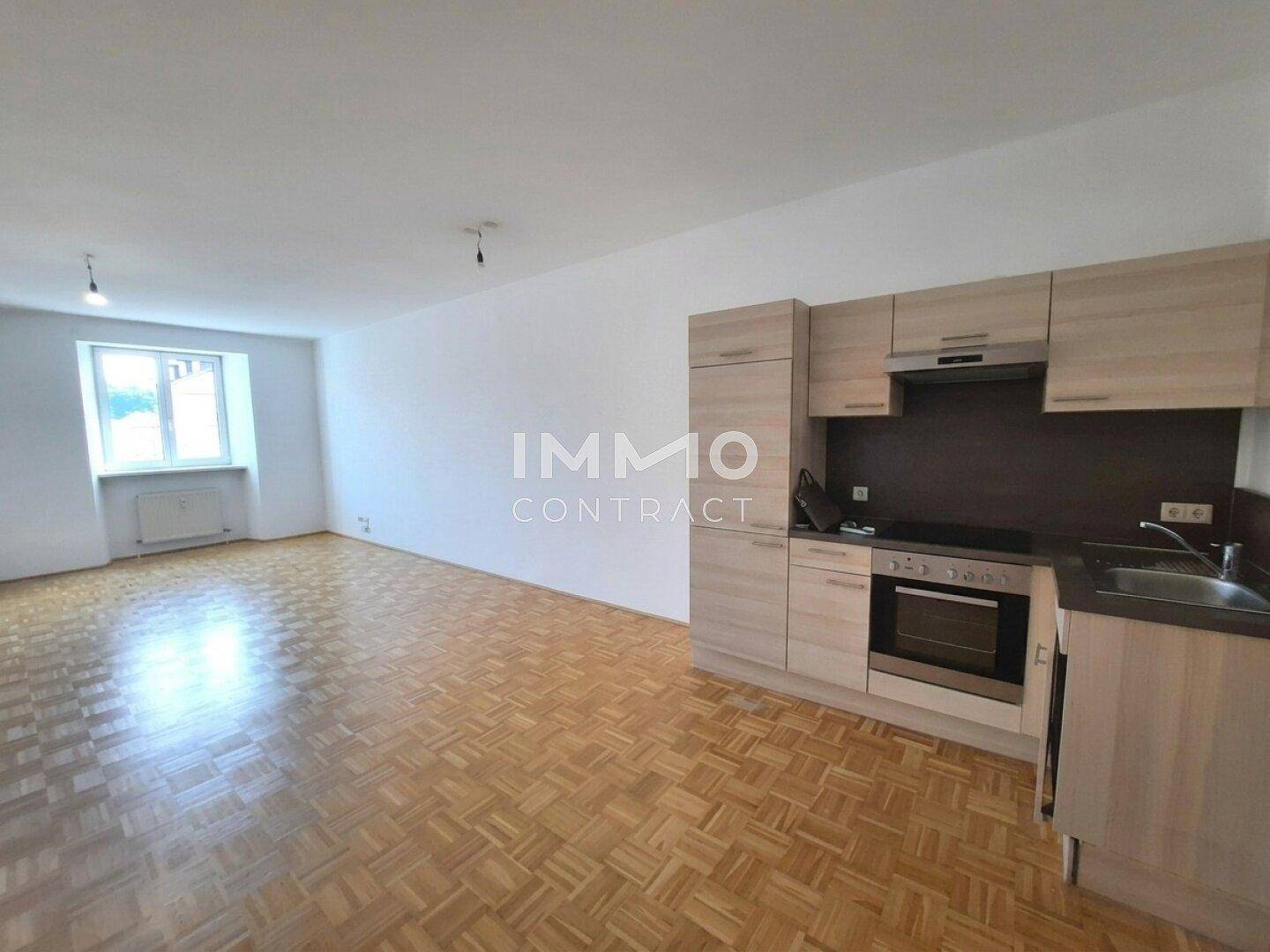 Heller Wohnbereich mit Parkettboden und integrierter Küchenzeile, ideal für ein Studio-Apartment.