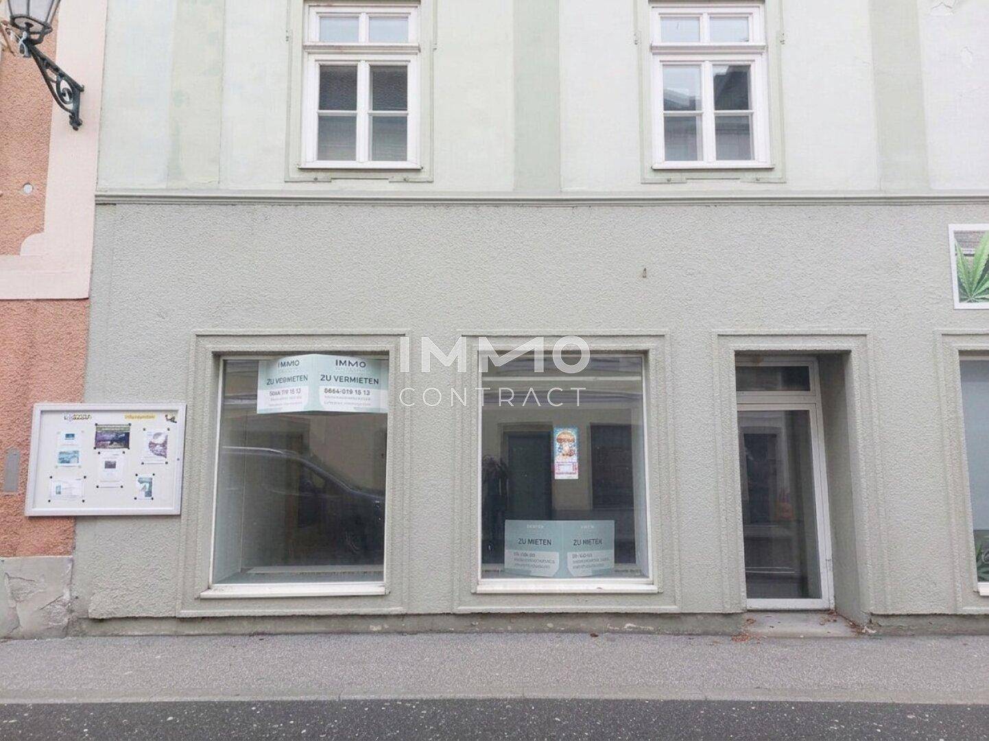 Nahaufnahme der Ladenfront im Erdgeschoss mit großen Schaufenstern und Vermietungsschildern.