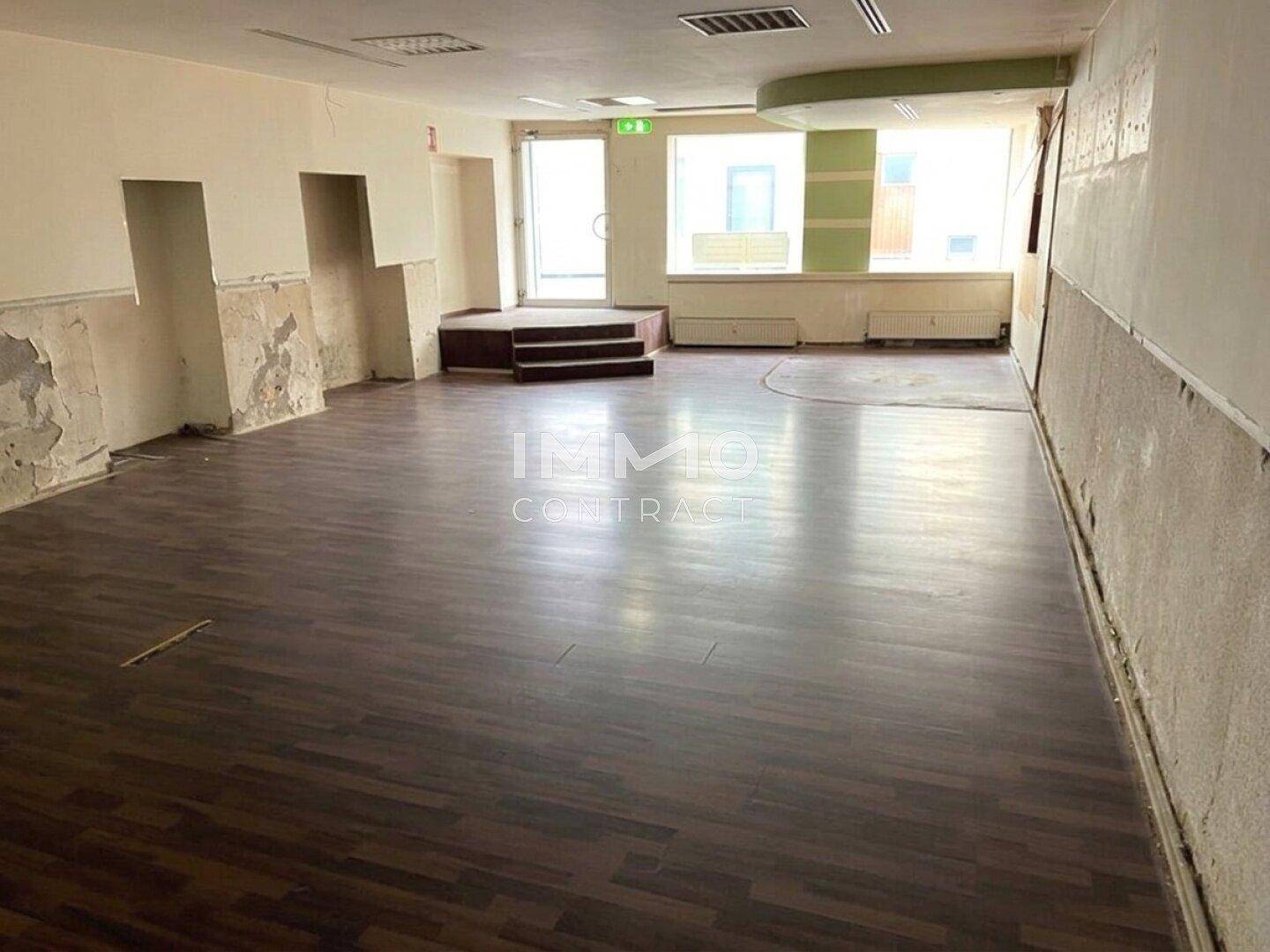 Geräumiger Innenbereich eines Gewerberaums mit Laminatboden und sichtbaren Abnutzungsspuren an den Wänden.
