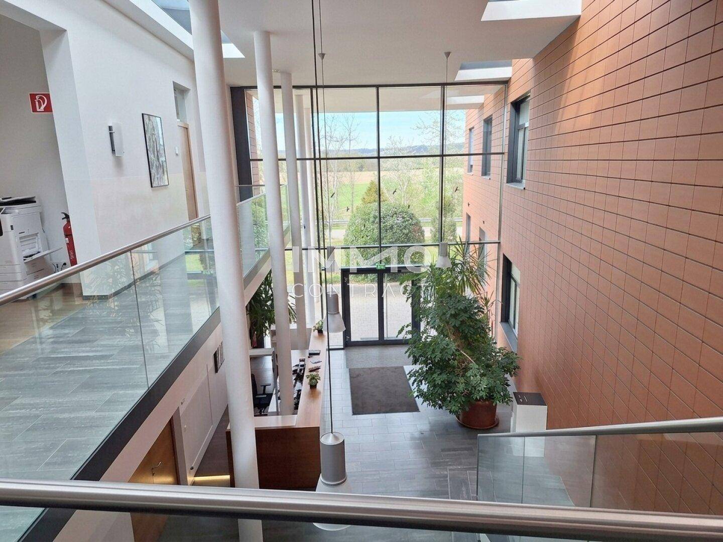 Geräumiges und helles Foyer mit hoher Decke, Glasfassade und Blick ins Grüne.