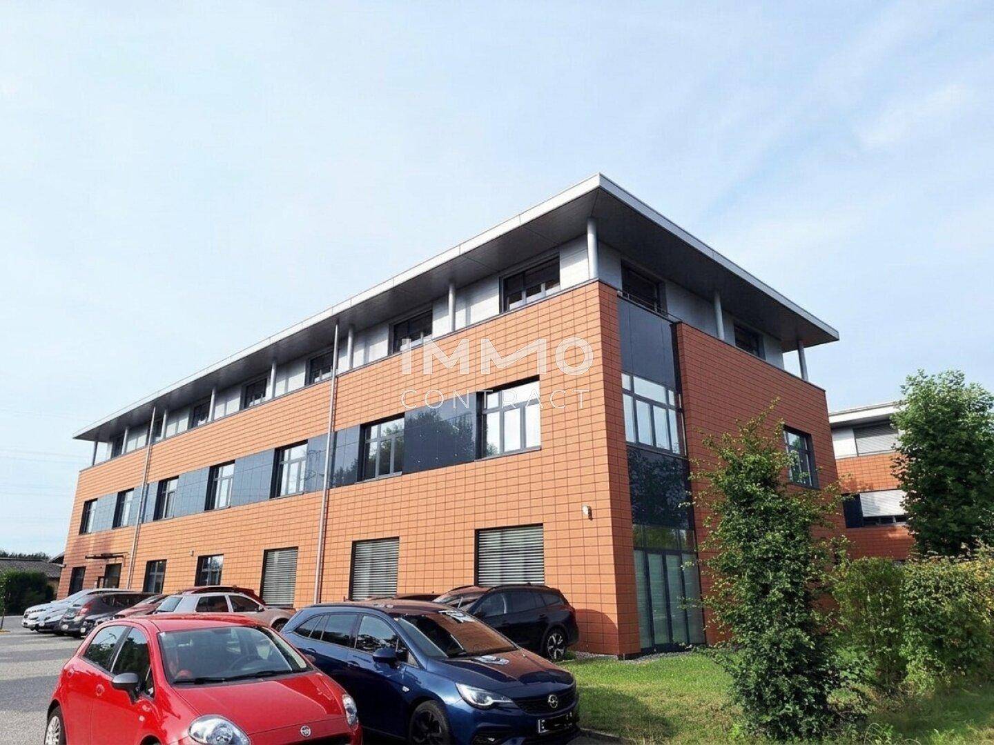 Ansicht des modernen Bürogebäudes mit orangefarbener Fassade und Parkplätzen im Vordergrund.