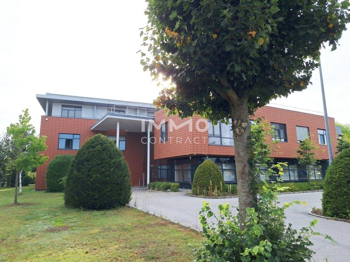 Eingangsbereich des modernen Bürogebäudes mit Zufahrt, Bäumen und gepflegten Grünflächen.