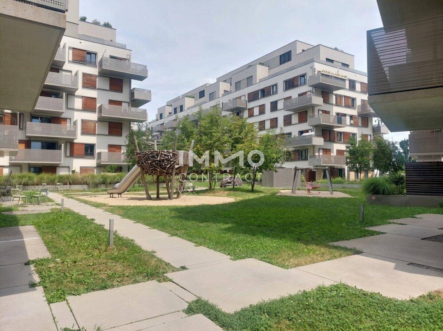 Weitläufiger Spielplatz mit Rutsche und Schaukel, umgeben von modernen Wohnkomplexen und Grünflächen.