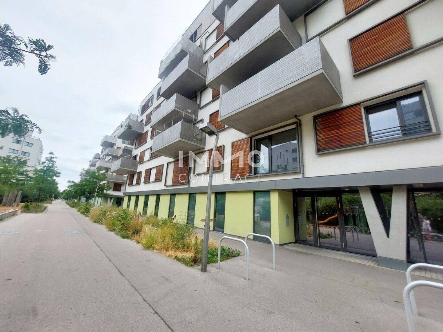 Moderne Wohngebäudeansicht von der Straße mit farbigen Akzenten im Erdgeschoss und zahlreichen Balkonen.