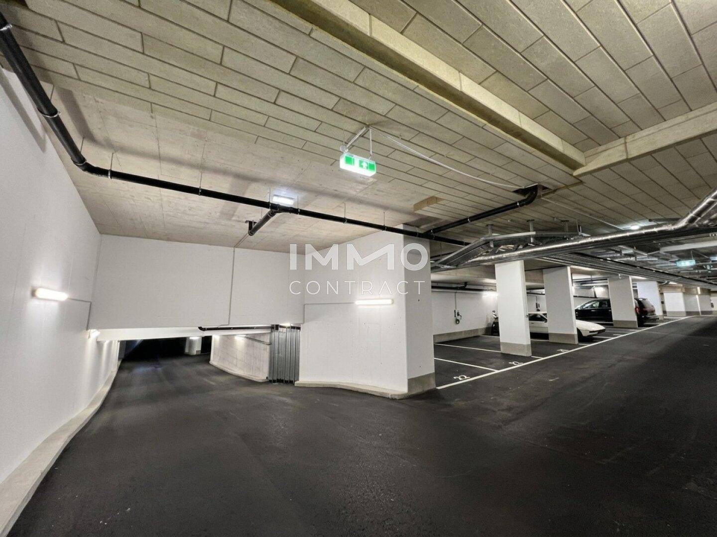 Moderne Tiefgarage mit markierten Stellplätzen, Betonpfeilern und sichtbaren Installationen sowie Ladesäulen.