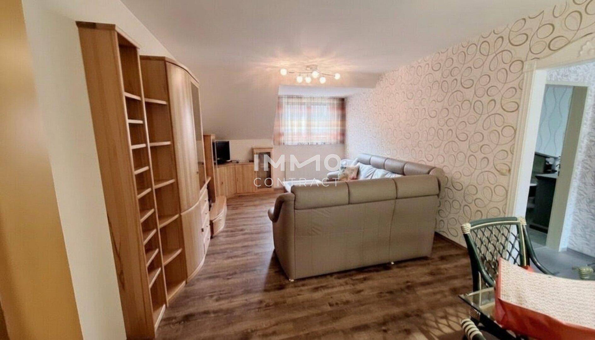Heller Wohnbereich mit Laminatboden, Holzmöbeln und bequemer Couch unter der Dachschräge.