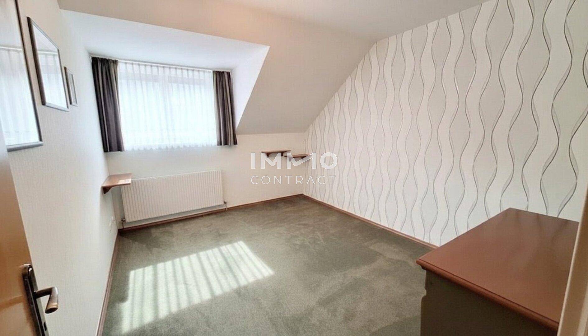 Schlafzimmer mit gemusterter Tapete, Teppichboden, Fenster und charakteristischer Dachschräge.