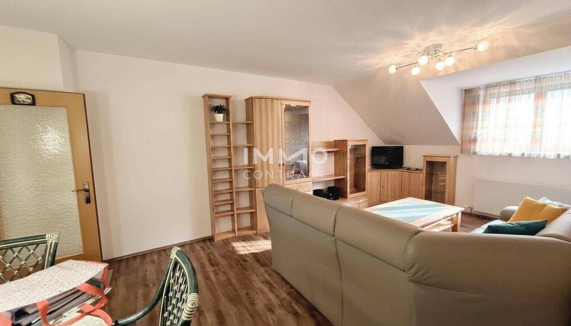 Gemütliches Wohnzimmer mit Laminatboden, beiger Couch, Holzmöbeln und Dachschräge.