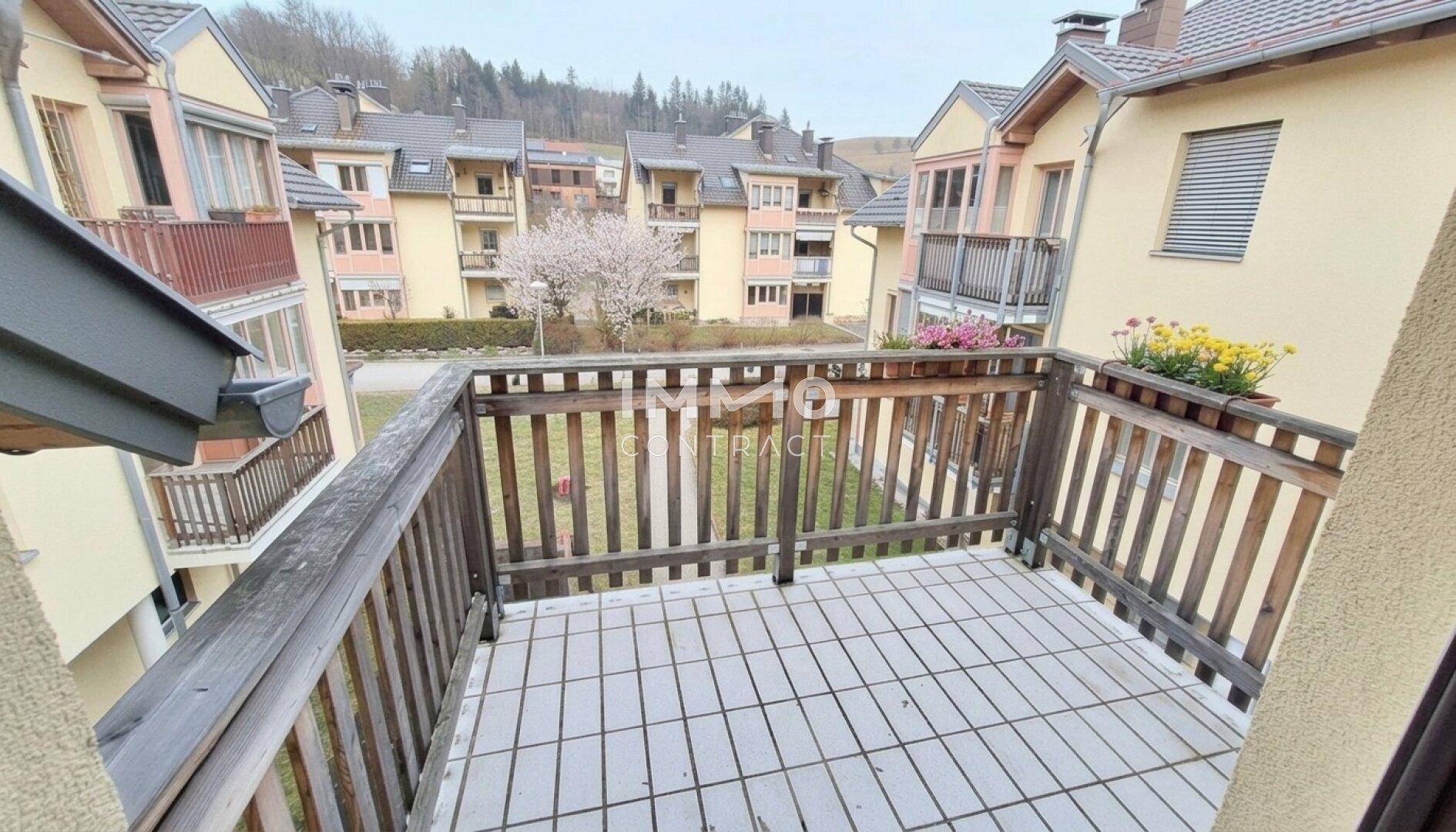 Balkon mit Holzbalken und Fliesenboden, bietet einen Blick auf die umliegenden Wohngebäude.