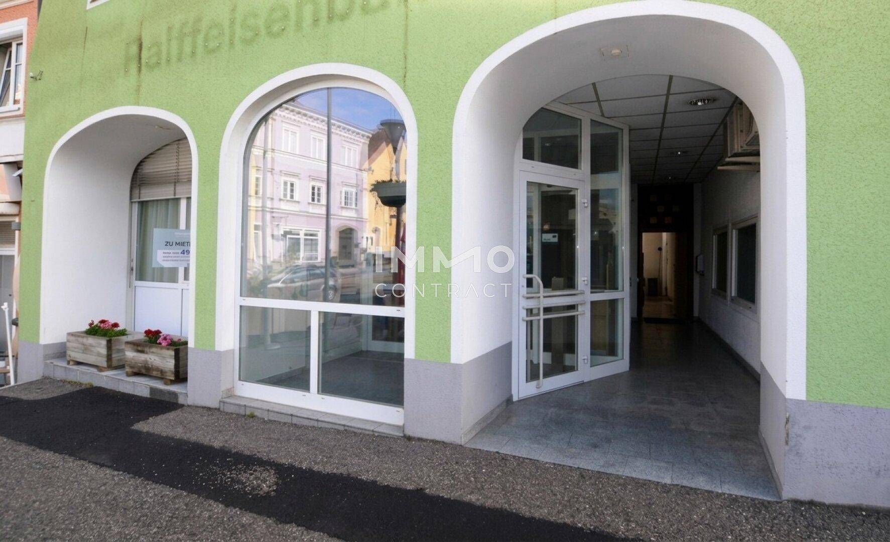 Grüne Gebäudefassade mit bogenförmigen Eingängen und großen Schaufenstern.