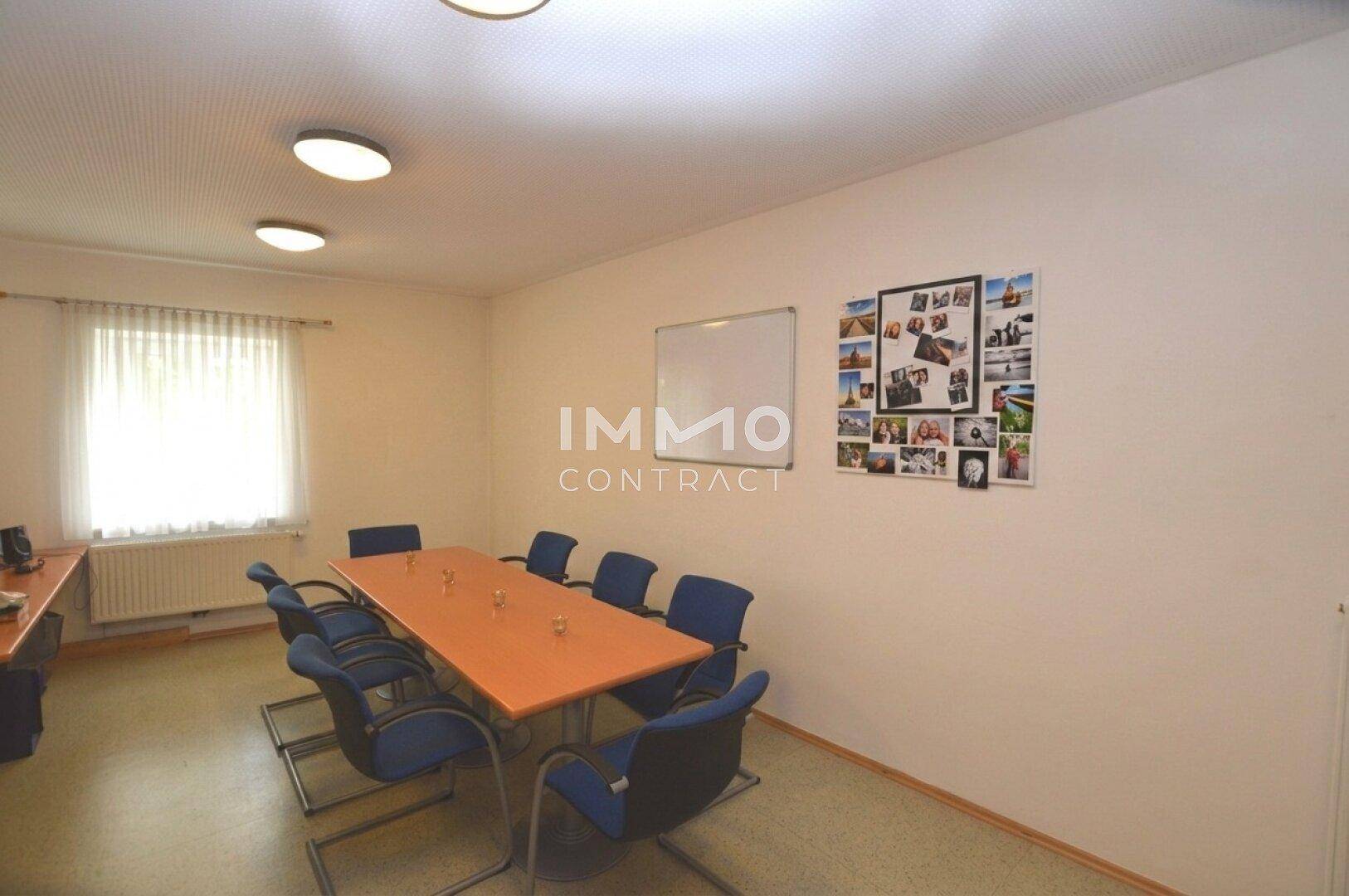 Konferenzraum mit langem Tisch, Stühlen, Fenster und Whiteboard an der Wand.